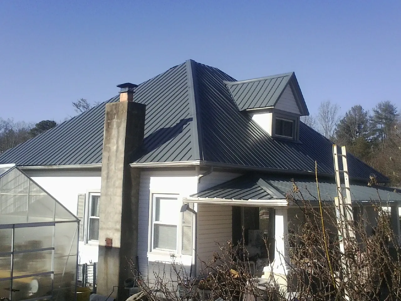 Dark blue standing seam metal roof on a white farmhouse with dormer — Slate & Tile Roof Repair by Roofing Brothers in Eastman