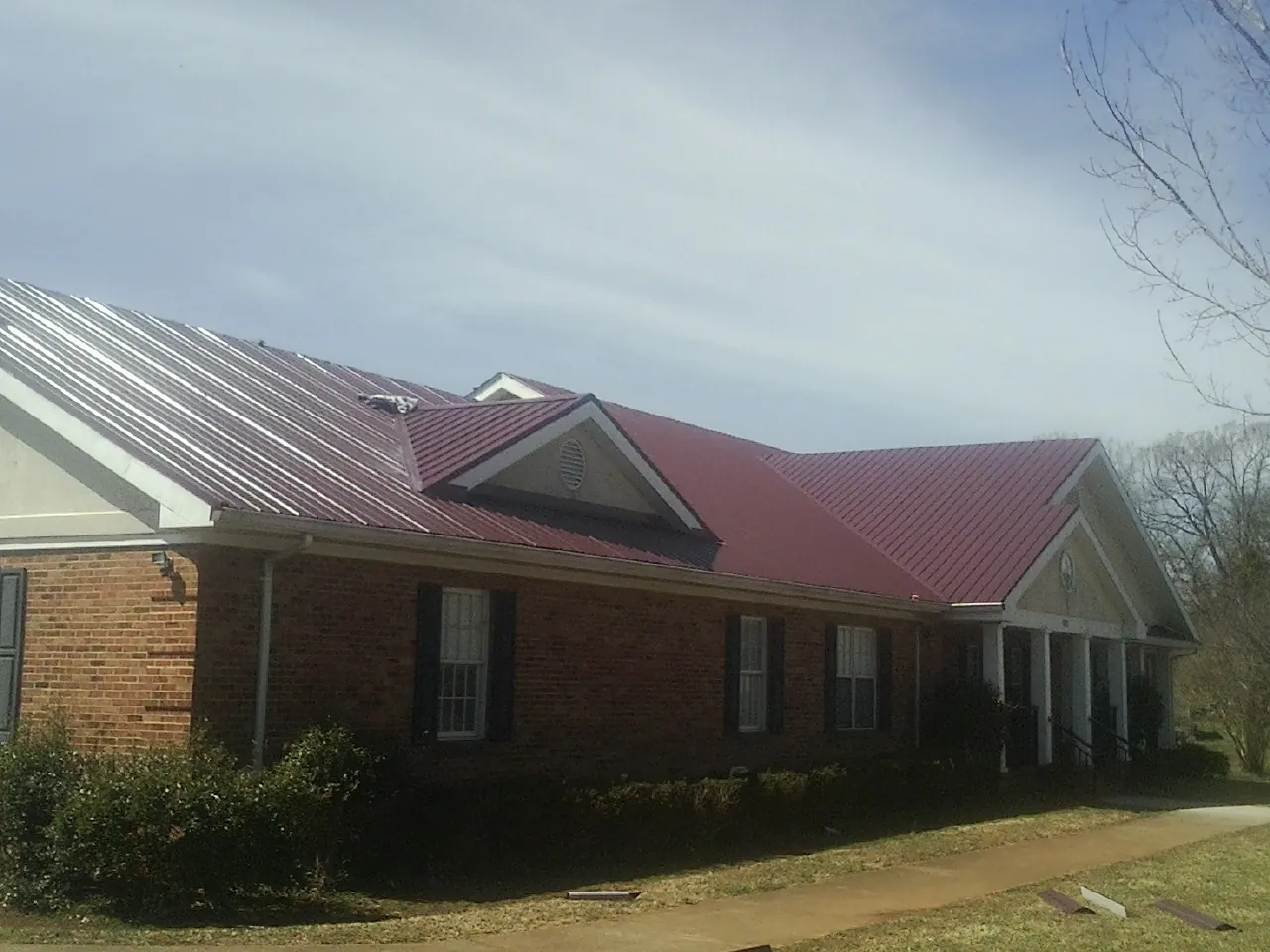 Red metal roof with gabled entries on a long brick building, from a Hail Damage Roof Repair job in Eastman