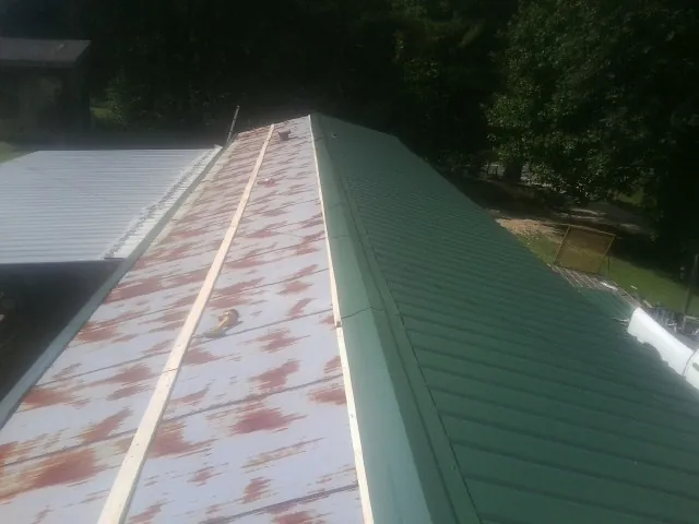 Old rusted panels beside newly installed green metal roofing — Wind Damage Roof Repair by Roofing Brothers in Eastman