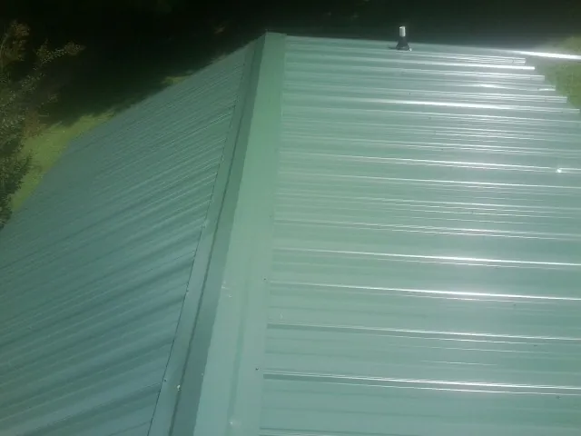 New green metal panels meeting at the ridge of a roof — Flat Roof Repair work by our crew in Eastman