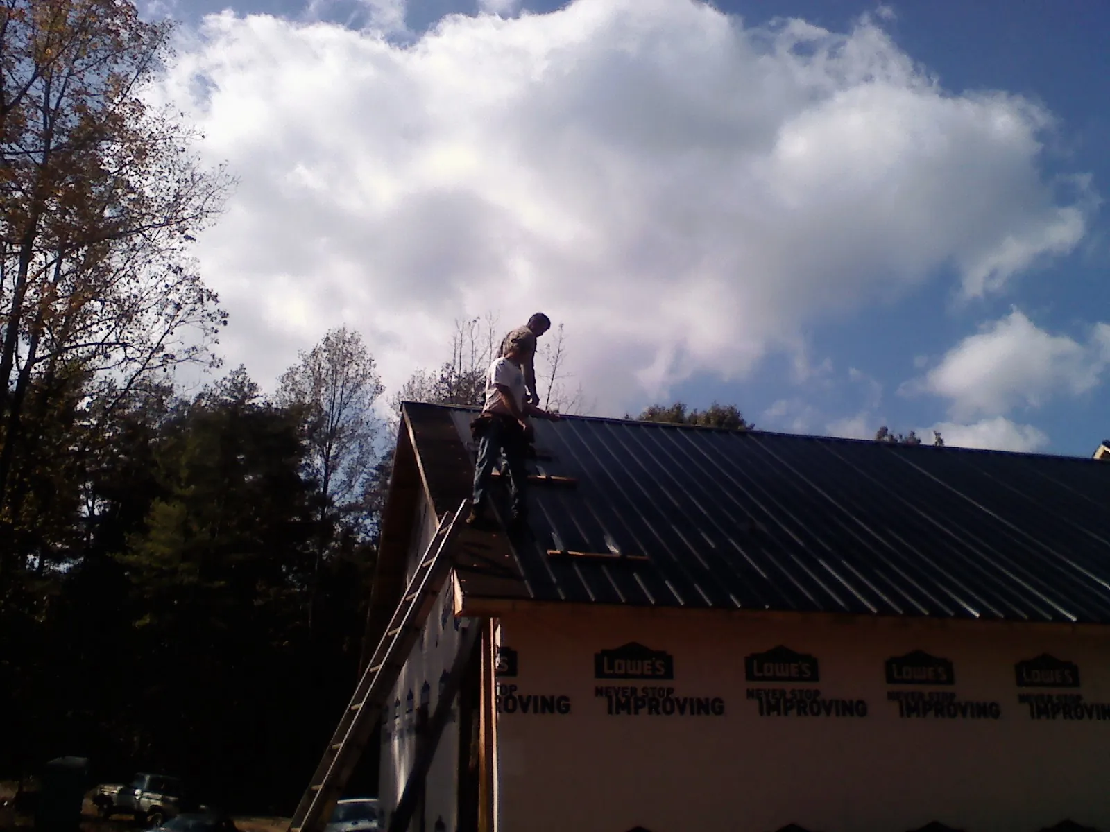 Roofer fastening dark metal panels high against a cloudy sky, from a Roof Inspection job in Eastman