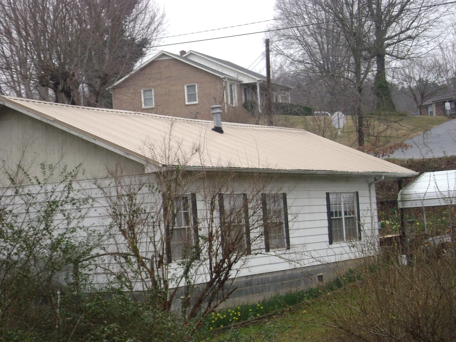 Tan metal roof on a white sided house set into a hillside — Commercial Roofing by Roofing Brothers in Eastman