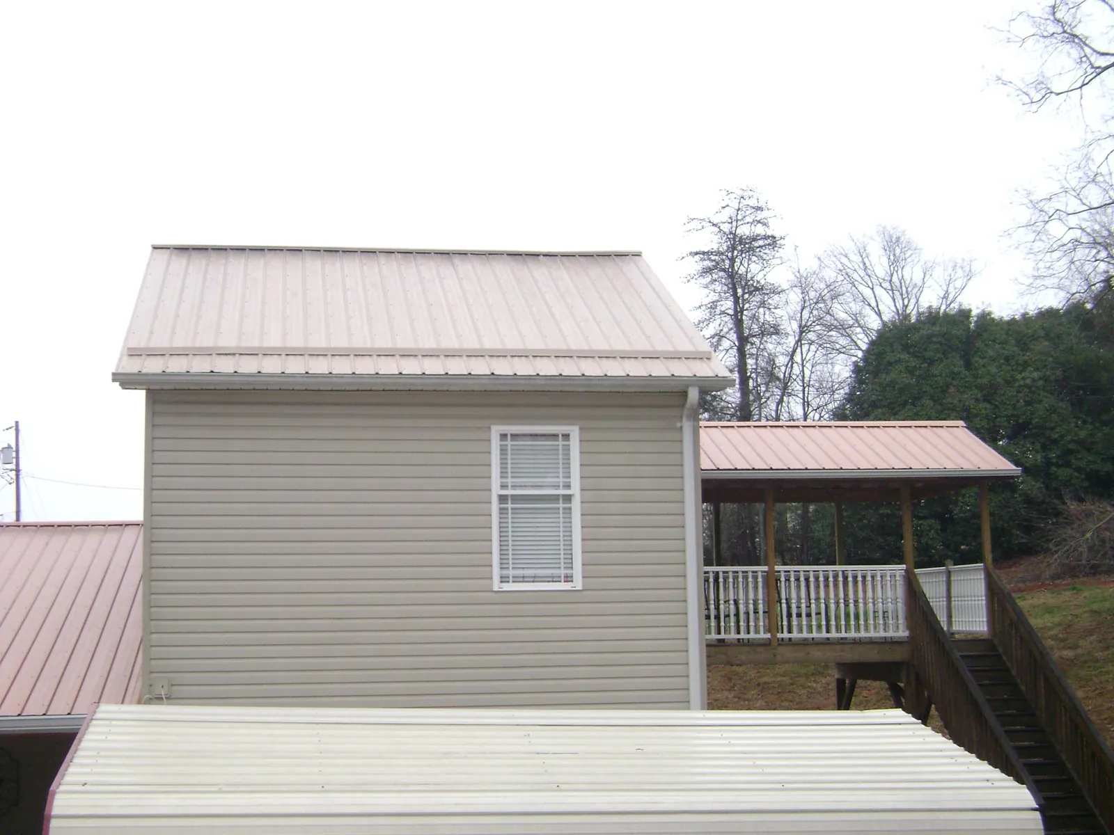 Tan metal roofs on a two story addition and attached porch, from a Roof Replacement job in Eastman